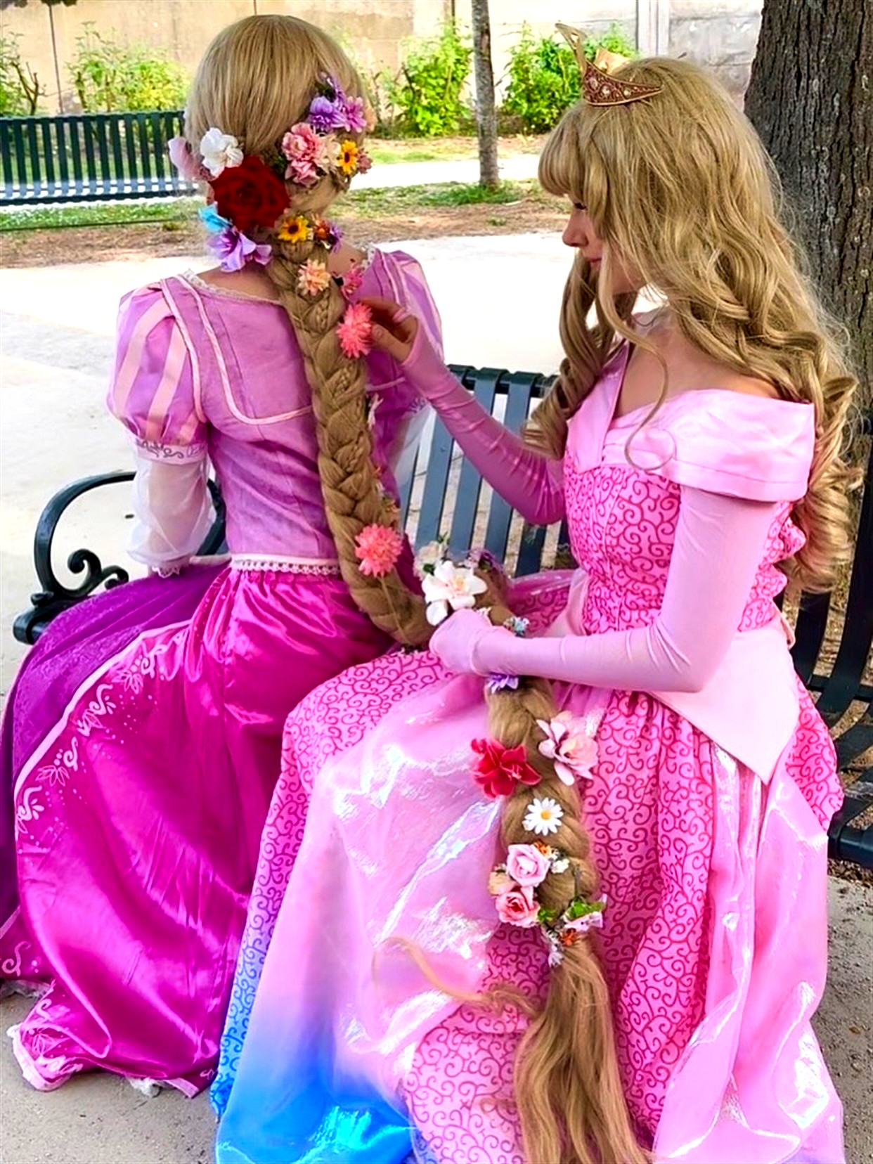 Animatrices costumées en Raiponce et Aurore assises sur un banc, tressant des fleurs dans les cheveux