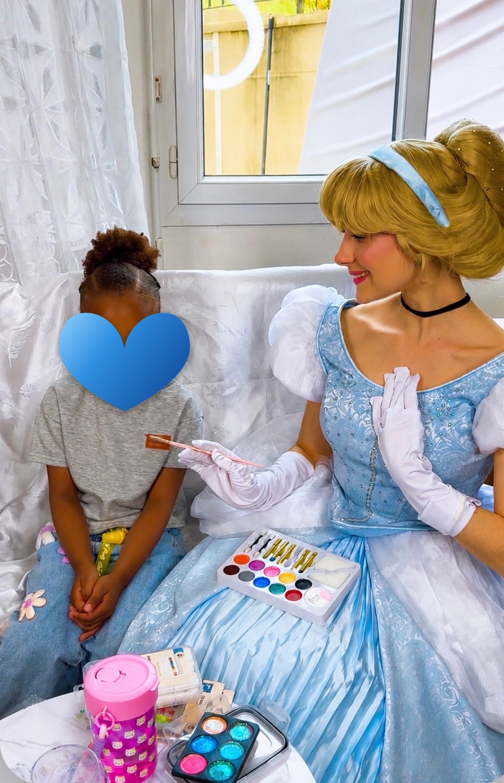 Animatrice costumée en Cendrillon maquillant une enfant lors d'un anniversaire à domicile